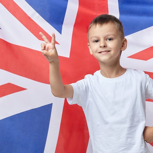 the cute boy folded his fingers in the shape of a V against the background of the British flag the cute boy folded his fingers in the shape of a V against the background of the British flag