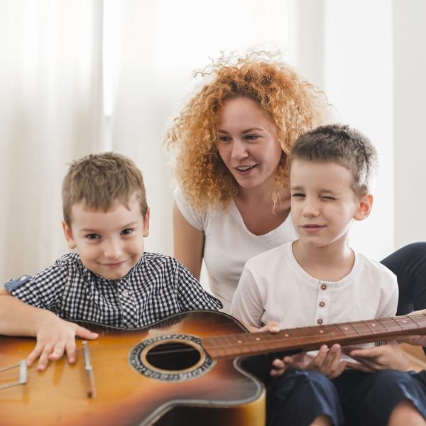 woman-sitting-with-her-children-playing-guitar woman-sitting-with-her-children-playing-guitar